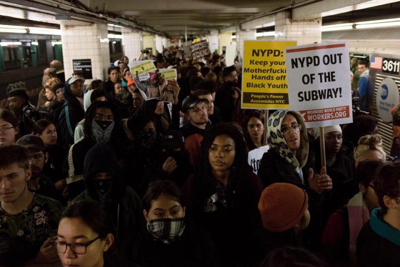 A protest in the NYC subway, with people holding signs that say "NYPD out of the subway."
