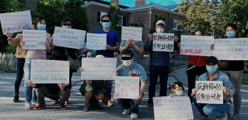 A group of Asian community members wearing masks and holding up signs in multiple languages with anti-trafficking messages written on them.