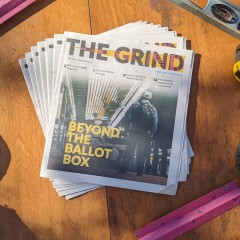 A photo taken from bird's-eye view. In the center, copies of an alt-weekly newspaper called The Grind are fanned out. The cover of The Grind shows a person standing in a subway station and the words