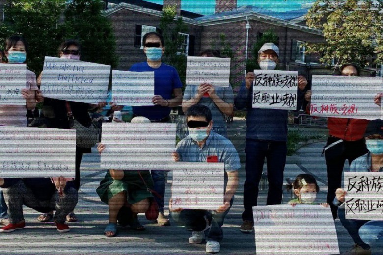 A group of Asian community members wearing masks and holding up signs in multiple languages with anti-trafficking messages written on them.