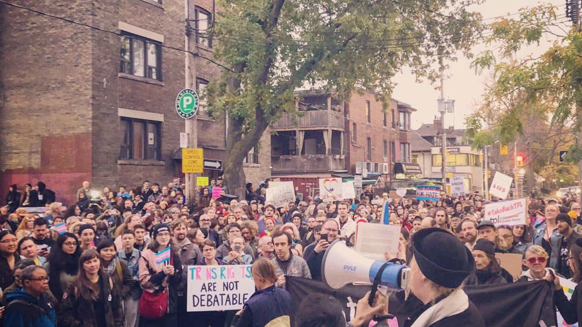 A photography of a crowd from above, listening to someone speak through a megaphone. One member of the crowd holds a sign that says "Trans rights are not debatable."